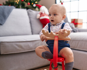 Sticker - Adorable caucasian baby playing with reindeer rocking by christmas tree at home