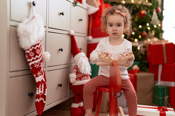 Sticker - Adorable caucasian girl playing with reindeer rocking by christmas tree at home