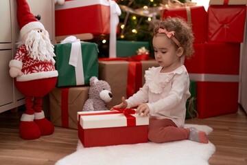 Sticker - Adorable caucasian girl unpacking gift sitting on floor by christmas tree at home