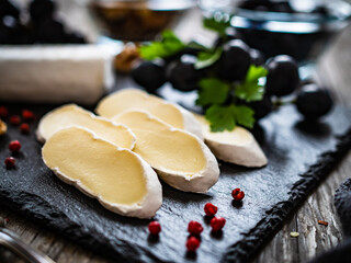 Wall Mural - Camembert cheese with grapes and walnuts on stony cutting board on wooden table
