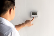 Close-up photo. The finger of a man's hand in a white shirt includes the buttons of the control panel of the air conditioner on the wall of the house, office.
