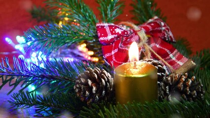 Wall Mural - Lit Gold Candle on green fir tree with pine cones. Christmas Sparkling lights and Decor on background. Effect of falling snow, Xmas Holidays atmosphere.