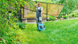 A man mows the lawn with an electric lawn mower in a landscaped garden. A man is tired from the tedious work of mowing the grass on the lawn on a hot summer day. Exhausting housework concept.