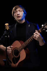 Male musician with guitar in hands playing and posing on black background in blue scenic light