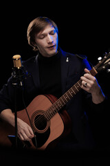 Male musician with guitar in hands playing and posing on black background in blue scenic light