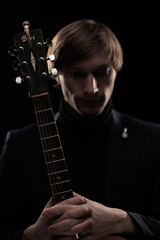 Male musician with guitar in hands playing and posing on black background in blue scenic light