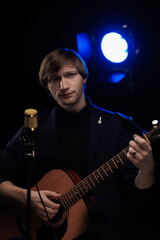 Male musician with guitar in hands playing and posing on black background in blue scenic light