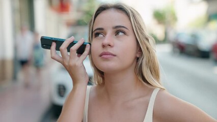 Poster - Young blonde woman listening audio message by the smartphone with serious expression at street