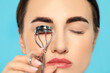 © New Africa - Woman using eyelash curler on turquoise background, closeup