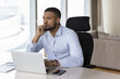 © fizkes - Happy millennial African freelance businessman looking away from office workplace, sitting at laptop computer on work table, thinking over project future vision, task completion