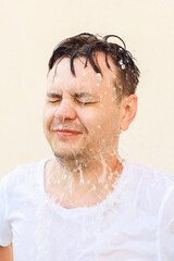 Wet young european white man in white t-shirt with closed eyes in water splash, water drops on yellow background. Portrait, stress shock concept, mental health, rain, emotions, face expression