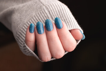 Wall Mural - Female hand in gray knitted sweater with beautiful manicure - blue glitter nails. Nail care concept