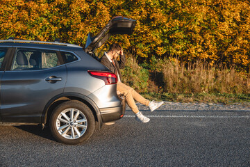 near the autumn forest, a man sits in the trunk of his car and rests after a long journey