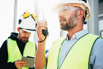 Male engeener wearing protect glasses and helment using walkie-talkie talking in production site. Team of structural engineers working on construction site