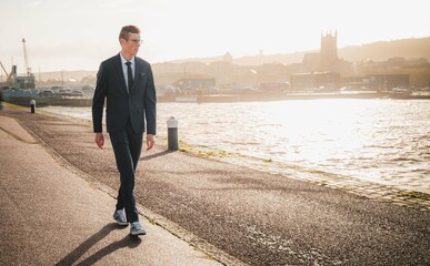 Young businessman casually walking in city on a bright sunny day. Young manager walking thinking about his business on docks by the sea