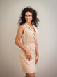 © George - A beautiful stylish young curly haired brunette female in a beige dress playfully posing in the photo studio. Portrait Studio Photography.