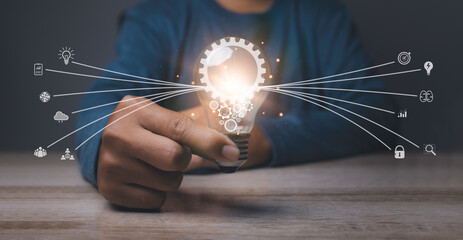 Wall Mural - Businessman holding a bright light bulb with gear icon and shining fibers in a shape of Idea