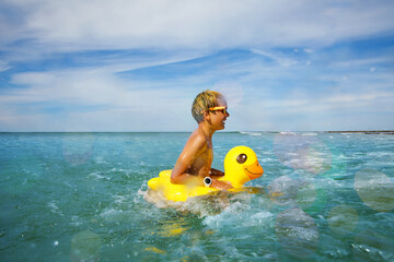 Wall Mural - Fun at ocean - boy in sunglasses swim with inflatable duck