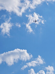 Wall Mural - The passenger airplane is flying far away in the blue sky and white clouds. Aircraft in the air. International passenger air transportation. The plane flies in the distance. Vertical illustration