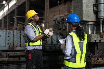 African American male engineer in vest and helmet safety operating control overhead crane for moving heavy metal at factory. Professional technicians in industrial machinery