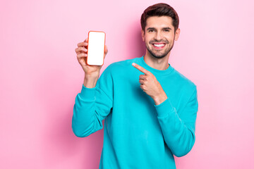 Photo of young toothy beaming smile guy student wear blue sweater hold phone finger direct empty space touchscreen isolated on pink color background