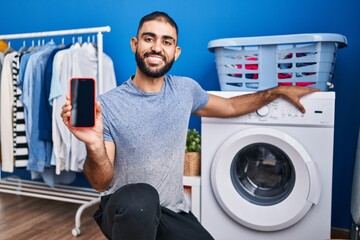 Canvas Print - Middle east man with beard showing smartphone screen and washing machine smiling with a happy and cool smile on face. showing teeth.