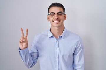 Wall Mural - Handsome hispanic man wearing business clothes and glasses showing and pointing up with fingers number two while smiling confident and happy.