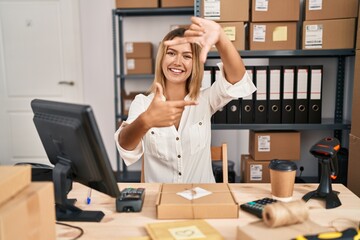 Wall Mural - Young blonde woman working at small business ecommerce smiling making frame with hands and fingers with happy face. creativity and photography concept.