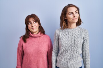 Canvas Print - Mother and daughter standing over blue background smiling looking to the side and staring away thinking.