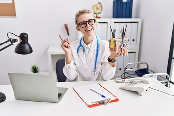 Sticker - Young doctor woman holding model of human anatomical skin and hair at the clinic smiling happy pointing with hand and finger to the side