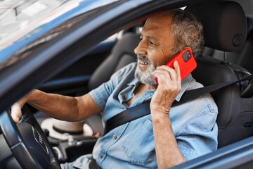 Wall Mural - senior grey-haired man talking on smartphone sitting on car at street