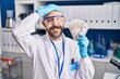 © Krakenimages.com - Young hispanic man working at scientist laboratory holding money stressed and frustrated with hand on head, surprised and angry face