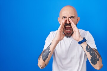 Sticker - Hispanic man with tattoos standing over blue background shouting angry out loud with hands over mouth