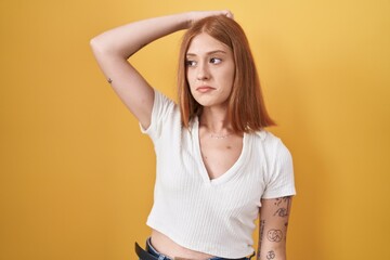 Poster - Young redhead woman standing over yellow background confuse and wondering about question. uncertain with doubt, thinking with hand on head. pensive concept.