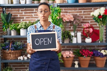 Canvas Print - African american woman working at florist holding open sign making fish face with mouth and squinting eyes, crazy and comical.