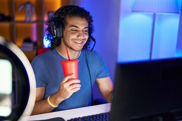 Poster - Young latin man streamer playing video game drinking beverage at gaming room