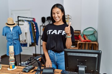 Sticker - Young hispanic woman working as staff at retail boutique doing happy thumbs up gesture with hand. approving expression looking at the camera showing success.