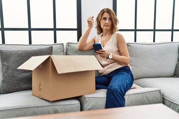 Poster - Middle age woman sitting on the sofa checking delivery package on the phone annoyed and frustrated shouting with anger, yelling crazy with anger and hand raised