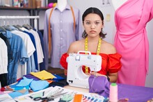 Hispanic Young Woman Dressmaker Designer Using Sewing Machine Relaxed With Serious Expression On Face. Simple And Natural Looking At The Camera.