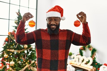 Canvas Print - Young african american man smiling confident holding balls standing by christmas hat at home