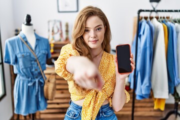 Poster - Young caucasian woman at retail shop using smartphone pointing with finger to the camera and to you, confident gesture looking serious