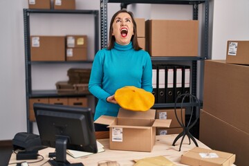 Canvas Print - Middle age hispanic woman working at small business ecommerce preparing order angry and mad screaming frustrated and furious, shouting with anger looking up.