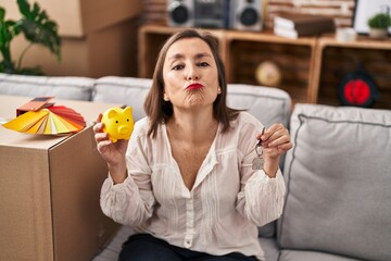 Sticker - Middle age hispanic woman holding piggy bank at new home looking at the camera blowing a kiss being lovely and sexy. love expression.