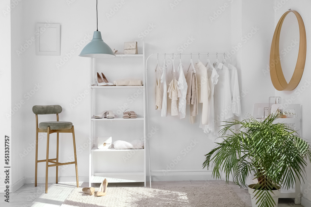 Interior of light dressing room with rack, clothes and shelving unit