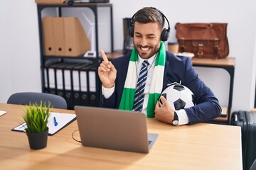 Sticker - Handsome hispanic man watching football game at the office smiling happy pointing with hand and finger to the side