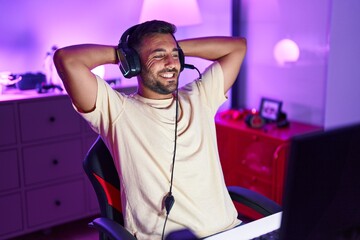 Young hispanic man streamer smiling confident relaxed with hands on head at gaming room