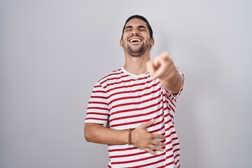 Wall Mural - Hispanic man with long hair standing over isolated background laughing at you, pointing finger to the camera with hand over body, shame expression