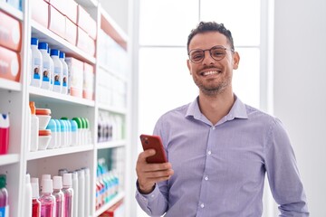 Sticker - Young hispanic man customer smiling confident using smartphone at pharmacy