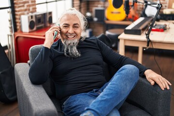 Sticker - Middle age grey-haired man musician talking on smartphone sitting on chair at music studio