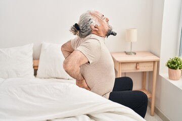 Canvas Print - Middle age grey-haired man suffering for back injury sitting on bed at bedroom